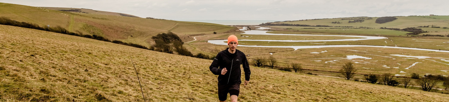 Ollie Goulden running the Downs above the Cuckmere meanders, the sea beyond